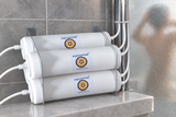 Aquadyne purifier resting flat on the bathroom shelf, all filters connected, beside a shower post